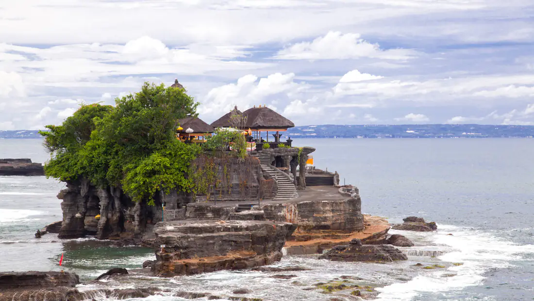 The Tanah Lot sea temple on its rocky outcrop surrounded by ocean waves under a cloudy sky in Bali