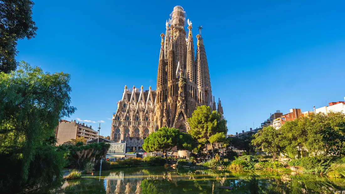 The Sagrada Familia basilica in Barcelona reflected in a park pond under a clear blue sky
