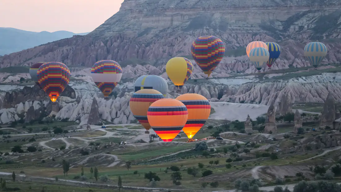 Colourful hot air balloons rising over the rock valleys and fairy chimneys of Cappadocia at dawn in Turkey